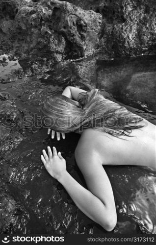 Young nude Asian woman lying face down on rocks.