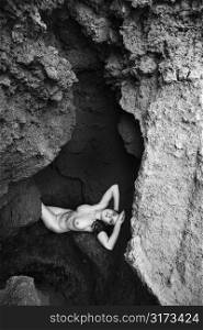 Young nude Caucasian woman lying down with hands behind head in a cave.