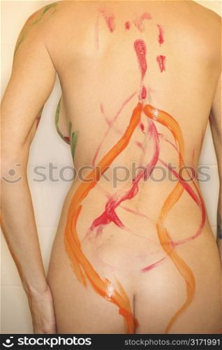 Young nude female Caucasian adult standing with paint on back.