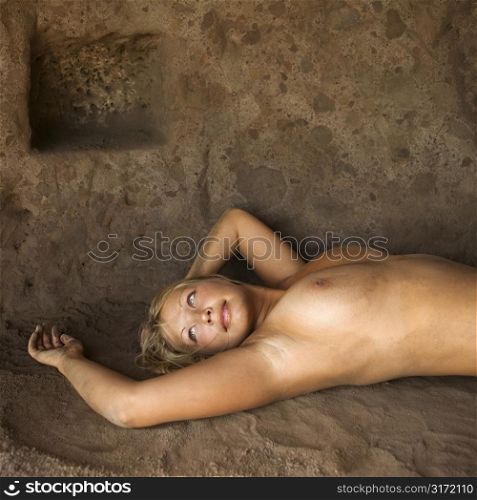 Young nude female reclining on back in cave.