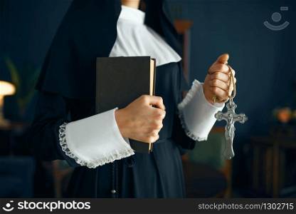 Young nun in a cassock with a cross around her neck holds a book. The sister is preparing for pray in the monastery. Young nun in a cassock holds book