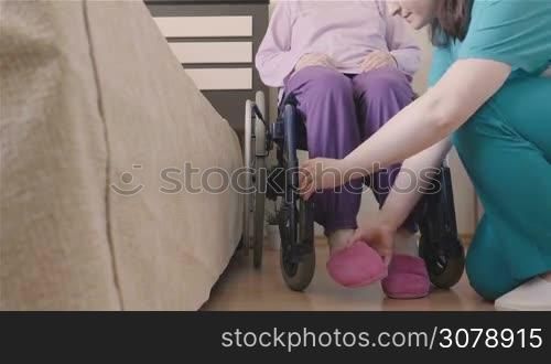 Young nurse caring of elder disabled woman in wheelchair and going for a walk. Home or hospice nursing and assistance concept.