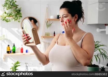 Young overweigh woman looking looking at the mirrow and examine her face. Wellness and body positivity. Young overweigh woman looking looking at the mirrow