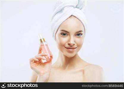 Young p≤asant looking woman uses perfum, likes≠w smell, stands delighted indoor, applies makeup, has hea<hy skin wears bath towel isolated on white background has glamorous look. P≤asant smelling