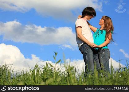 young pair holds each other in grass against sky