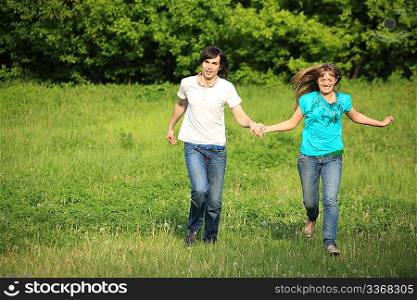 young pair runs, keeping for hands, on grass in park