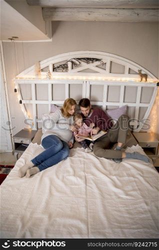 Young parent reading book to cute little girl in bed at home