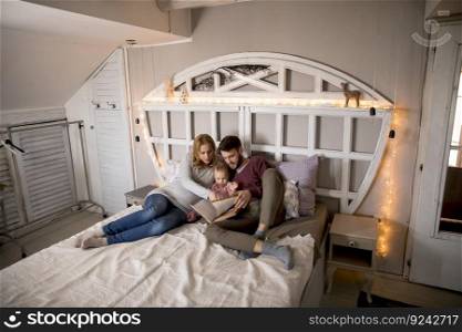 Young parent reading book to cute little girl in bed at home