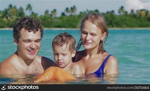 Young parents and little son bathing in sea. Father and son holding starfish, dad showing it