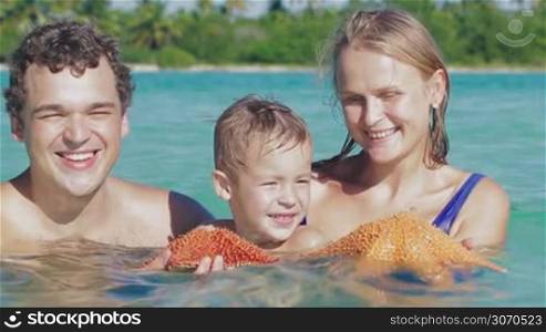Young parents and little son bathing in sea, they holding starfish or sea star