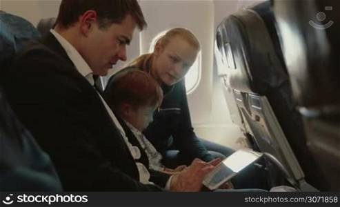 Young parents and little son in the plane. Child playing with cell phone, mother talking to father using tablet computer