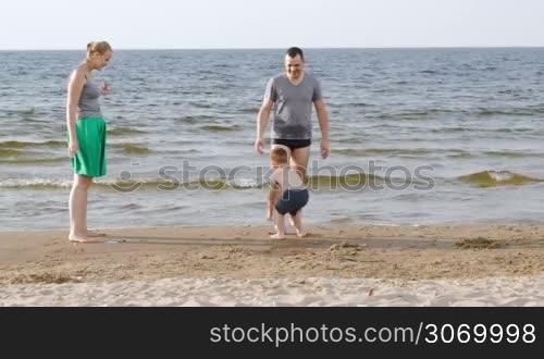 Young parents and little son playing ball on the beach at seaside
