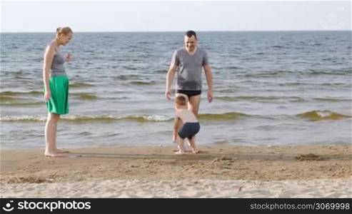 Young parents and little son playing ball on the beach at seaside