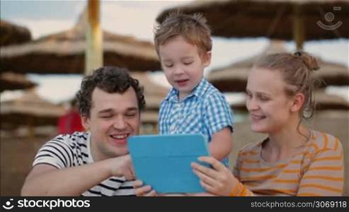 Young parents and their cute little son using touchpad on the beach