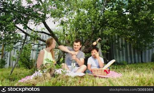 Young parents and their son during the picnic in the courtyard. Mother and father drinking wine, boy eating apple