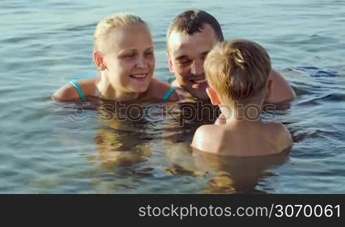 Young parents lying in sea water and giving son small stones from the bottom