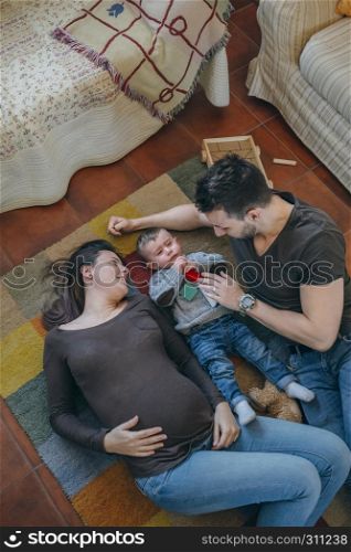 Young parents playing with their sad little son in the living room while they comfort him. Parents playing with their sad little son in the living room
