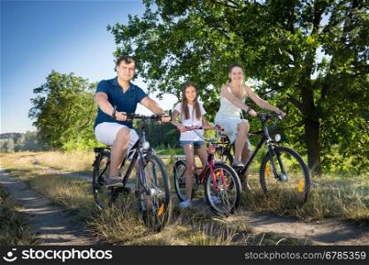 Young parents riding on bicycles with their daughter at meadow