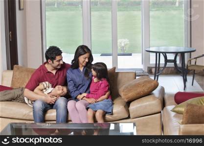 Young parents sitting with kids on sofa at home