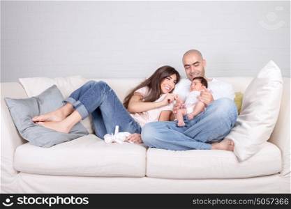 Young parents with little baby at home, sitting on cozy divan, enjoying family, loving couple with newborn daughter, positivity and fun concept