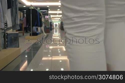 Young parents with little child walking through the family clothing store. they passing by racks with jeans, shirts and t-shirts
