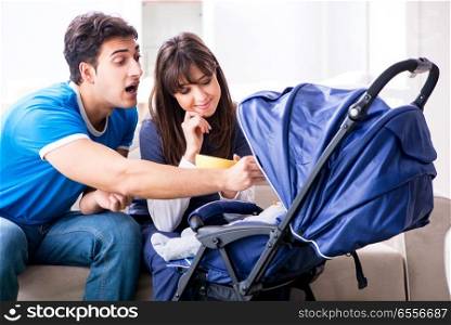 Young parents with their newborn baby in baby pram sitting on th. Young parents with their newborn baby in baby pram sitting on the sofa