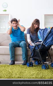 Young parents with their newborn baby in baby pram sitting on the sofa