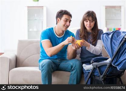 Young parents with their newborn baby in baby pram sitting on the sofa