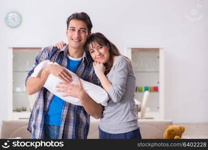 Young parents with their newborn baby near bed cot