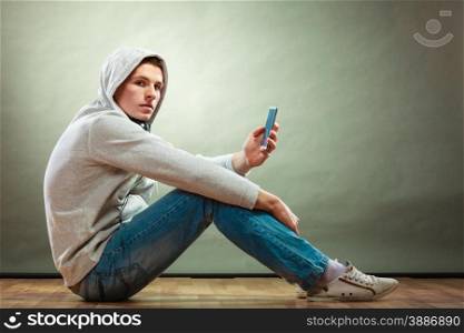 Young people and leisure concept. hooded man teen boy with headphones sitting on floor listening music grunge background