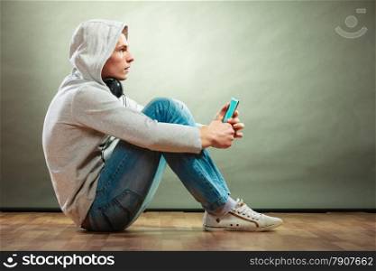 Young people and leisure concept. hooded man teen boy with headphones sitting on floor listening music grunge background