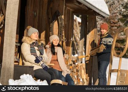 Young people by wooden winter cottage enjoying sunshine outdoor