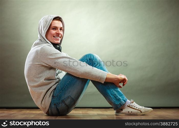 Young people concept. Smiling hooded man teen boy with headphones sitting on floor grunge background