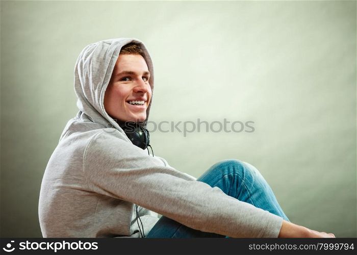 Young people concept. Smiling hooded man teen boy with headphones sitting on floor grunge background