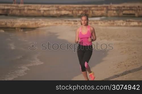 Young people doing sport activity, girl running on the beach, woman jogging near the sea. Leisure, healthy recreation, sports exercising, training, working out. Slow motion at sunset