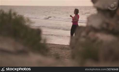 Young people doing sport activity, girl running on the beach, woman jogging near the sea. Leisure, fitness, recreation, sports exercising, training, working out. Female athlete stretching, slow motion