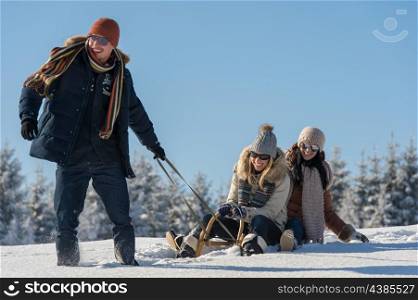 Young people enjoy sunny winter day sledge man pulling girlfriends