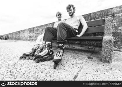 Young people friends in training suit with roller skates. Woman and man relaxing on bench outdoor.. Young people friends relaxing on bench.