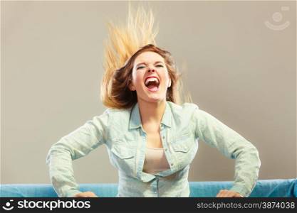 Young people happiness concept. Fashionable girl wearing denim relaxing on blue couch wind in hair face expression