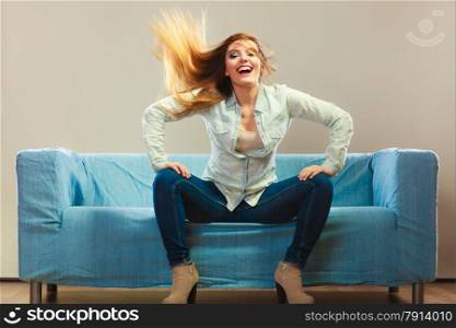 Young people happiness concept. Fashionable girl wearing denim relaxing on blue couch wind in hair