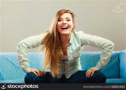 Young people happiness concept. Fashionable happy girl wearing denim sitting on blue couch