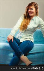 Young people happiness concept. Fashionable happy girl wearing denim sitting on blue couch
