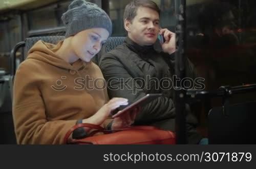 Young people in the bus. Woman uisng tablet PC and man talking on the phone during evening traveling in the city