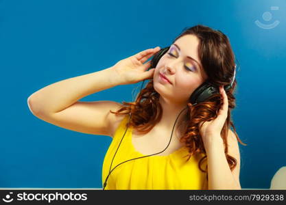 Young people leisure relax concept. Closeup teen cute girl in big headphones listening music mp3 relaxing on blue background