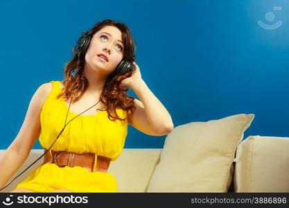 Young people leisure relax concept. Teen cute girl yellow dress in big headphones listening music mp3, sitting on couch relaxing on blue