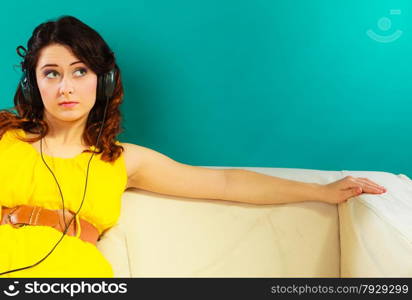 Young people leisure relax concept. Teen cute girl yellow dress in headphones listening music mp3, sitting on couch relaxing green blue background