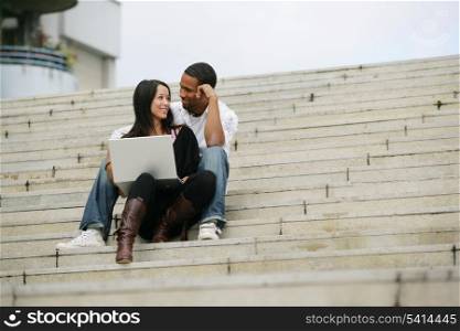 Young people sitting on steps of stairs with laptop