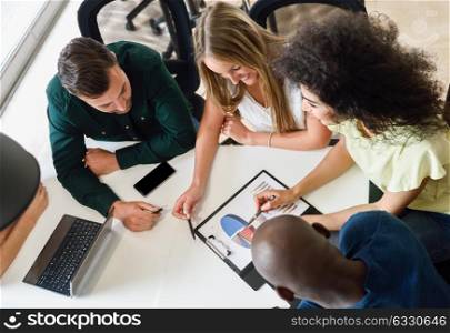 Young people studying with laptop computer on white desk. Beautiful women and men working together wearing casual clothes. Multi-ethnic group. Top view