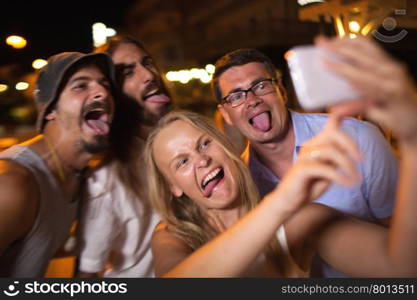 Young people taking crazy selfie with mobile. Young friends with funny faces making smart phone selfie at night. They fooling and putting out tongues