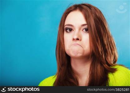 Young people teenage concept - teen funny girl making silly face, unhappy face expression on blue